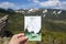 The travel postcard in the hand with background of mountains, adventures in the mountains, enjoy the moment