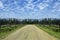 Travel road on the field with green grass and blue sky with clouds on the farm in beautiful summer sunny day. Clean, idyllic, lan