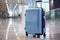 Travel Suitcase. Blue wheeled suitcase standing on the floor in airport terminal. Copy space. Travel background.