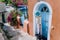 Travel tourist woman on vacation in Greece. Person with blue sunhat in front of traditional Mediterranean house. Colored