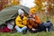 Travel, trekking and hiking concept - couple of hikers drinking tea or coffee near green tent in autumn forest