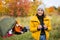 Travel, trekking and hiking concept - portrait of beautiful woman with binoculars near green tent in autumn forest