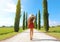 Travel in Tuscany. Young woman walking in beautiful and idyllic landscape of a lane of cypresses in the Italian countryside of