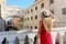 Travel in Venice. Back view of pretty girl in elegant red dress holding hat looking at Bridge of Sighs in Venice, Italy. Beautiful