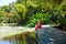 Travel woman in red dress relax in tropical resort. Female traveler on exotic summer vacation. Girl in straw hat sitting