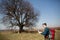 A traveler with a backpack, looking at the map and walking in the countryside. Tree in the background