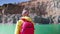 Traveler examines the area. View from the back. Stylish guy with a red backpack dressed in a yellow raincoat stands