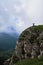 Traveler girl and her German Shepherd together on top of steep cliff against background of fog and sky before rain enjoy views and