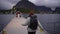 A traveler girl, sporting a hat and backpack, is depicted from behind as she heads towards the pier on the Lofoten