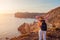 Traveler hiking by White beach on Aegean sea Santorini island, Greece enjoying landscape. Woman backpacker raised arms