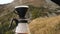 Traveler man making filter coffee and pours water in ground coffee beans against mountain view