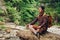 Traveler man in a meditative position with a backpack sitting on a tree trunk against the background of the forest and