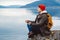 Traveler man in a meditative position sitting on a rocky shore on the background of a mountain and a lake. Space for