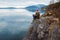 Traveler man in a meditative position sitting on a rocky shore on the background of a mountain and a lake. Space for