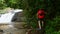 Traveler Man in Red T-Shirt Climbing on Stones with Bag on Cascade Waterfall