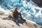 Traveler man with a yellow backpack wearing a red hat sitting on a rock on the background of a glacier and snow. Travel lifestyle