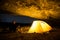 Traveler near the glowing camping tent in the night grotto under a starry sky