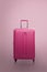 Traveler pink suitcase or cabin size luggage on pink background