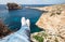 Traveler`s feet in white sneakers on the edge of rocky seaside