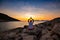 Traveler sits on the rock seashore and practicing yoga during sunset