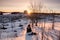 Traveler sitting on snowy with camera on tripod and sunrise on white house