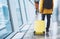 Traveler tourist in bright jacket with yellow suitcase backpack at airport on background large window blue sky, man waiting in dep