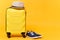 Traveler tourist suitcase trunk luggage bag with summer hat and sneakers isolated on yellow orange background. Passenger