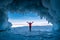 Traveler woman wear red clothes and raising arm standing on frozen water in ice cave at Lake Baikal, Siberia, Russia