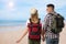 Travelers with backpacks on sandy beach near sea during summer vacation trip, back view. Space for text