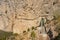 Travelers walking on a suspension road along a sheer cliff. Caminito del Rey. Dangerous trail in mountains. Railway bridge and tun