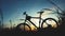 Traveling by bike. A silhouette of a bicycle stands in a field among grass on a sunset background. Soft golden fill