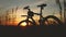 Traveling by bike. A silhouette of a bicycle stands in a field among grass on a sunset background. Soft golden fill