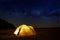 Traveling and camping concept - camp tent at night under a sky full of stars. Orange illuminated tent. Beautiful nature - field,