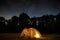 Traveling and camping concept - camp tent at night under a sky full of stars. Orange illuminated tent. Beautiful nature - field,