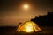 Traveling and camping concept - camp tent at night under a sky full of stars. Orange illuminated tent. Beautiful nature - field,