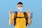 Traveling during covid-19 pandemic. Millennial guy with camping gears wearing mask, pointing up over blue background.
