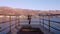 Traveling girl jacket stands on old pier in the sun on cool day, zoom in