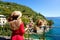 Traveling by Italy. Back view of pretty girl in red dress and hat looking houses on overhanging cliffs in Portofino, Italy.