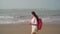 Traveling young woman with backpack walking along sea coast. Female tourist reading and examining map while resting on