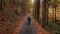 Traveller in a blue jacket walks along a forest path surrounded by orange fallen leaves