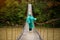 Traveller senior beautiful woman in blue rain jacket cross river by hinged bridge in forest, enjoying nature