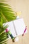 Travellers notebook with markers and pen on sand with palm tree leaf background, top view. Planning and ideas vacation concept.