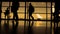 Travellers with suitcases and baggage in airport walking to departures in front of window, silhouette, warm