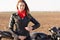 Travelling on bike. Serious beeautiful cool motorcyclist zips black leather jacket, has red bandana on neck, enjoys long route on