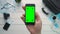 Travelling concept Top view traveler`s hand holding phone vertical with green screen and tracking points at white wooden