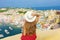 Travels in Italy. Back view beautiful young woman with hat sitting on wall looking at stunning panoramic view of Procida Island,
