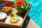 Tray with assorted breakfast meal and drinks near swimming pool