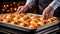 Tray with freshly baked golden pastry and bakers hands