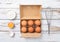 Tray with organic brown eggs with yolk,whisk and shell on white wooden background