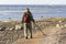 A treasure hunter with a metal detector walks along the sandy deserted beach in search of lost coins